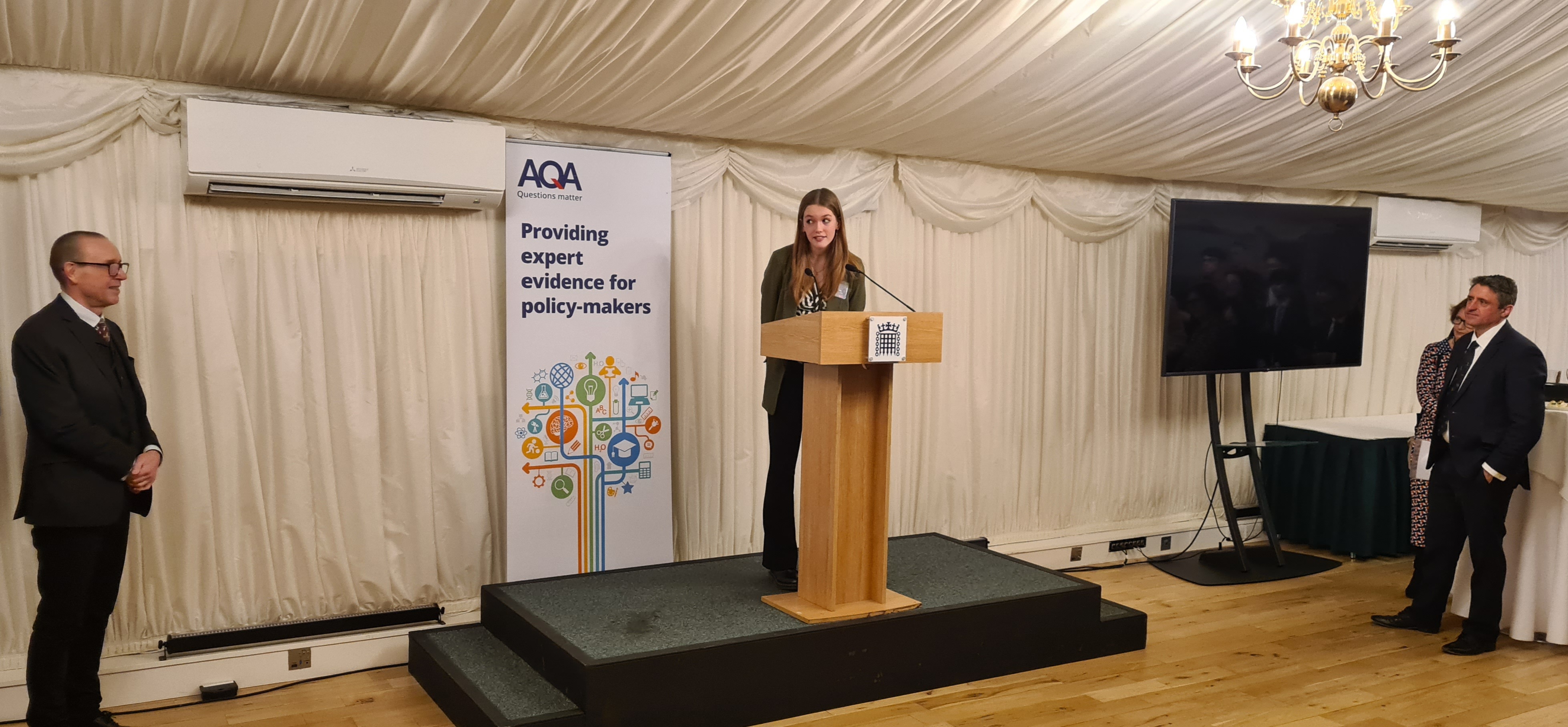 Cerys McGrath speaking with AQA CEO Colin Hughes (far left) and event sponsor, Ben Everitt MP(far right), listening intently.